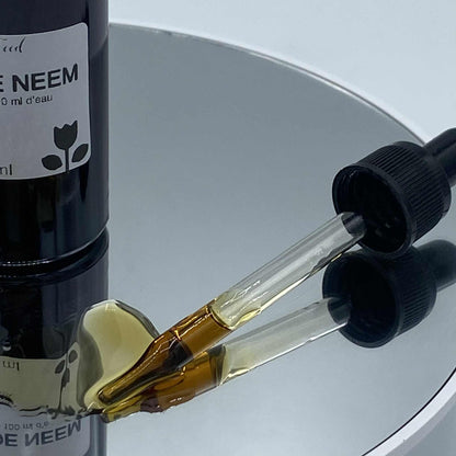 Gros plan sur un flacon d'huile de neem avec une pipette contenant un liquide ambré, posé sur une surface réfléchissante.